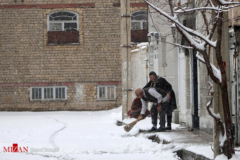 پیرمرد و پیرزن ابهری که مشغول برف روبی دم در خانه خود هستند.