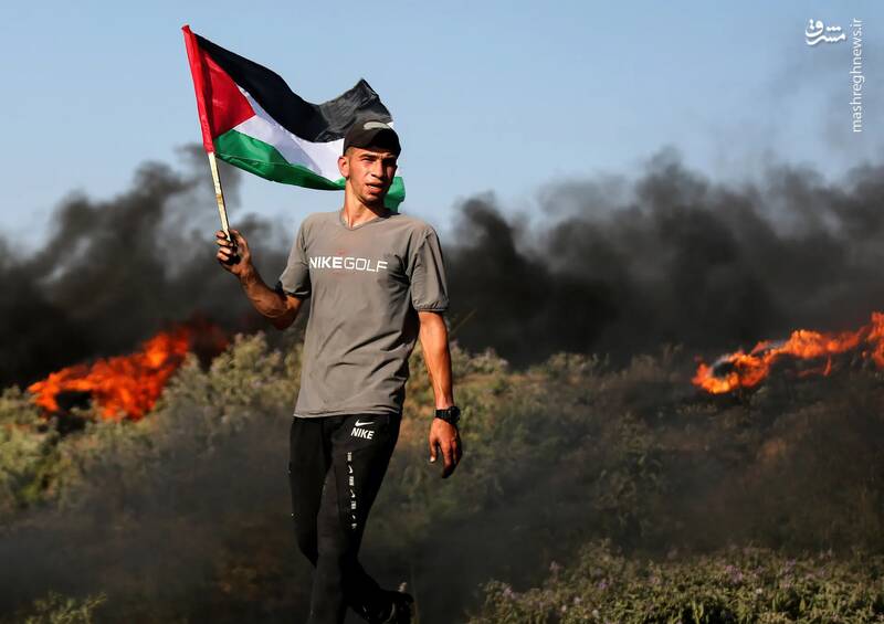 یک فلسطینی پرچم کشورش را در میان لاستیک‌های سوخته در نزدیکی حصار مرزی با اسرائیل در شرق شهر غزه در جریان اعتراض به حمله نظامی اسرائیل به جنین در کرانه باختری به دست دارد.