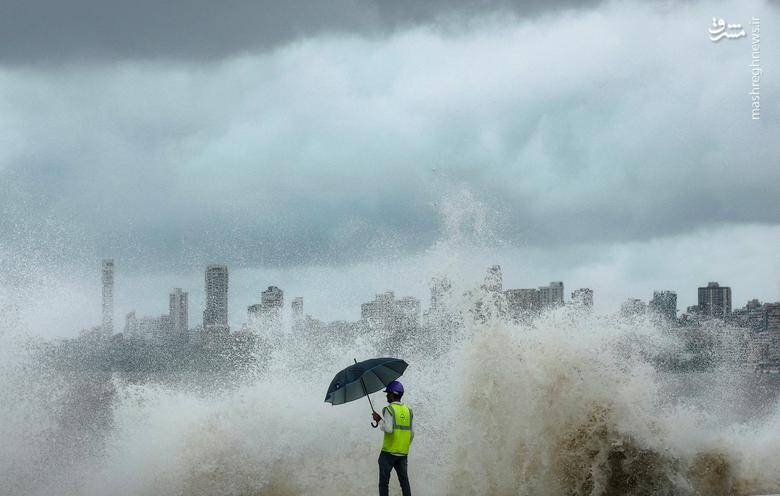 یک کارگر ساختمانی شاهد برخورد امواج به سازه ساحلی و جزر و مد دریا در بمبئی _ هند است.